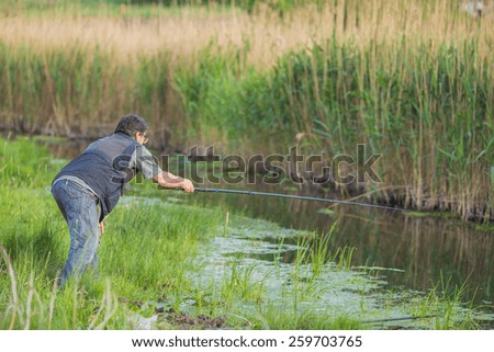 Fisherman on the river bank. Man fisherman catches a fish. Fisherman in his hand holding spinning. Fishing, spinning reel, fish. The concept of a rural getaway. Article about fishing.