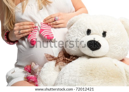 A woman holds her baby pink toe pregnant belly and soft toy bear