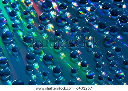 Water drops on reflective surface. Hard lighting produces rainbow-like effect on the background and the drops themselves. Light bounces everywhere and is refracted as it passes through the drops.