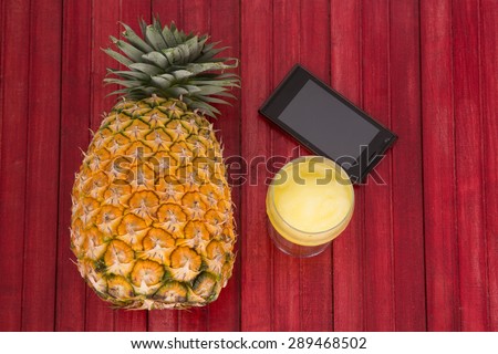 Fresh  pineapple and pineapple juice and smart phone on red wood table