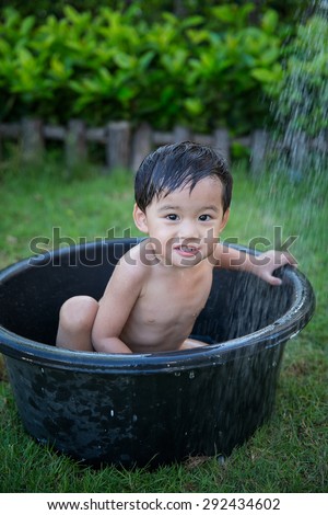 Asian baby boy taking bath in a black basin in garden