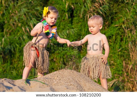 Young children are a boy and girl playing in the sand by the sea in comic costumes - skirts the wild tribes. Summer.
