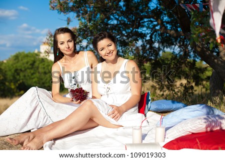 Two young beautiful girlfriends resting under a tree in the heat of summer.