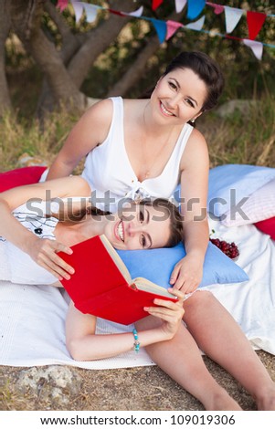 Two young beautiful girlfriends resting under a tree in the heat of summer.