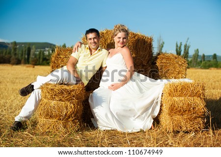 Beautiful couple pregnant wife and husband enjoyed the stay on a yellow field on a background of blue sky and hay. Summer.