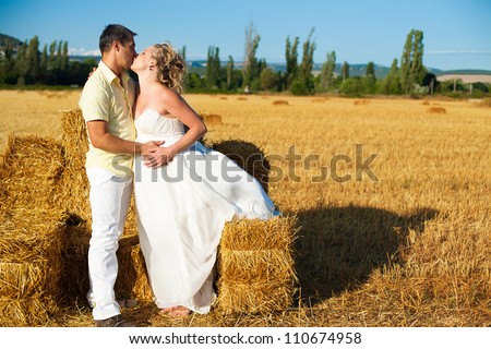 Beautiful couple pregnant wife and husband enjoyed the stay on a yellow field on a background of blue sky and hay. Summer.