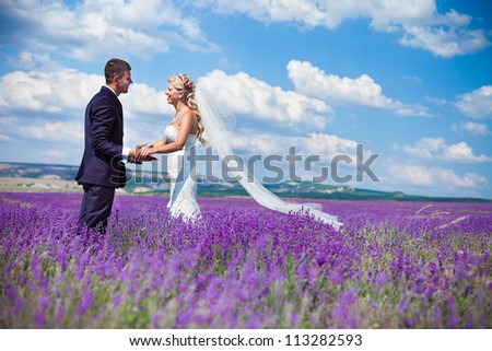 A young couple in love bride and groom, wedding day in summer. Enjoy a moment of happiness and love in a lavender field. Bride in a luxurious wedding dress on a background bright blue sky with clouds.