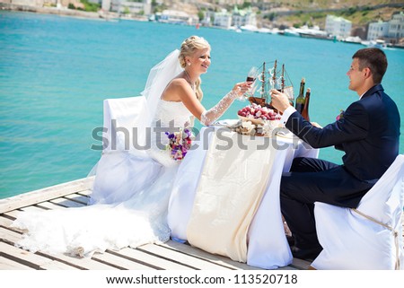 Beautiful couple in love the bride and groom posing on the bridge at the sea at the wedding table decorated with exotic bottles and wooden model ship. Enjoy a moment of happiness and love.