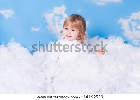 Beautiful baby girl with angel wings in white clothes posing on a background of the sky with clouds - decorated in the style of a little angel in the clouds. A series of photos in my portfolio.