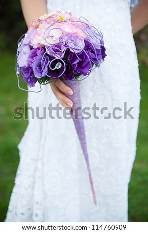 Wedding bouquet of purple and pink flowers in the hands of the bride