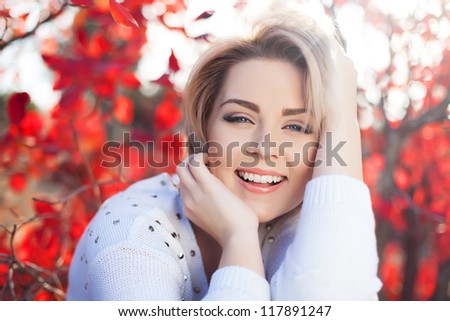 Portrait of a beautiful young and healthy woman with blonde hair and expressive eyes bob. Posing in the park against the tree with bright red leaves. Autumn.
