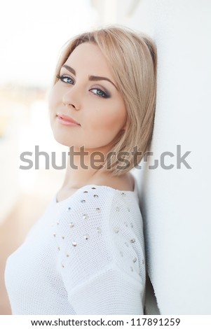 Portrait of a beautiful young and healthy women blonde with expressive eyes and a bob hairstyle. Poses in front of a white wall.
