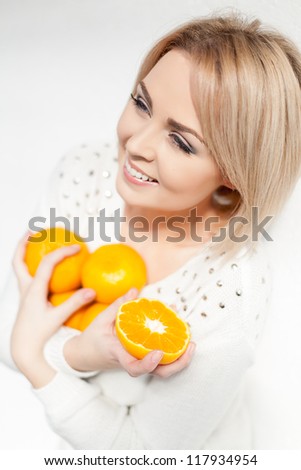 Portrait of a beautiful young and healthy women blonde with expressive eyes and a bob hairstyle. Poses in front of a white wall with yellow tangerines in hands.