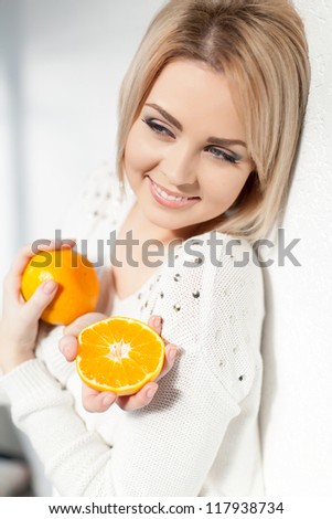 Portrait of a beautiful young and healthy women blonde with expressive eyes and a bob hairstyle. Poses in front of a white wall with yellow tangerines in hands.