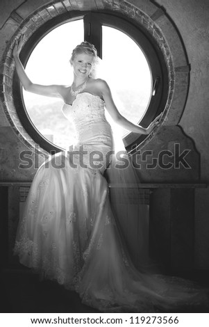 Portrait of a beautiful young bride sitting on a window sill round window.