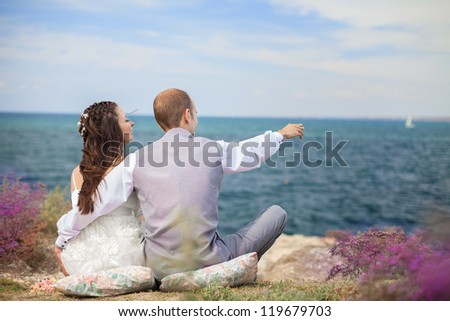 The bride and groom are sitting back watching the sea. Enjoy a moment of happiness and love in their wedding day.