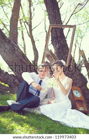 Portrait of the bride and groom are posing with the big frame in the park.
