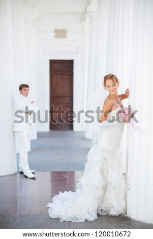 Young couple in love bride and groom posing near the white columns, standing at a distance from each other in their wedding day in summer.