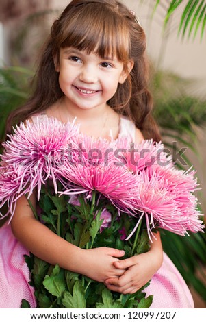 Beautiful little girl posing with a large bouquet of flowers in a luxurious pink dress at home.