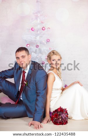 Young couple in love bride and groom posing in studio on background decorated with Christmas tree in their wedding day at Christmas. Enjoy a moment of happiness and love.