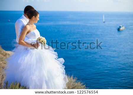 Couple in love young bride and groom dressed in white hugging on cliff background of blue sea in their wedding day in summer