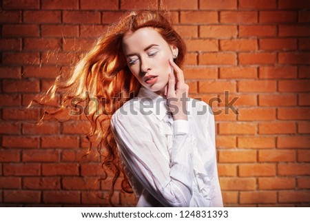 Portrait of fashionable woman with long red hair in motion over wall backgroun
