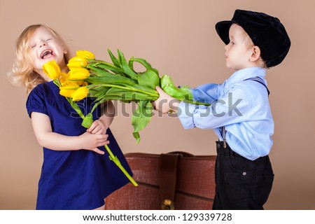 Funny kids, happy little boy giving a cute girl bouquet of yellow spring flowers. Series in studio. Valentines Day