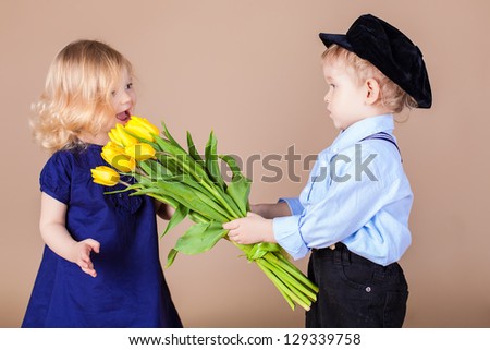 Funny kids, happy little boy giving a cute girl bouquet of yellow spring flowers. Series in studio. Valentines Day