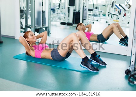 Gym fitness woman working out doing press fitness exercise smiling happy during workout. Young fitness model training in fitness center.