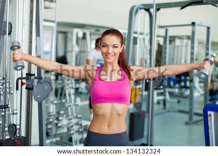 Gym fitness woman working out doing weight training smiling happy during workout. Young fitness model training in fitness center.