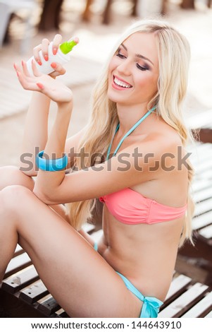 Sunscreen woman. Young happy girl putting sun block on beach holding white sun tan lotion bottle