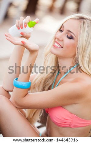 Sunscreen woman. Young happy girl putting sun block on beach holding white sun tan lotion bottle