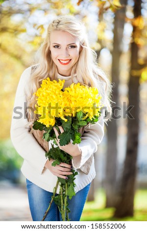 Young woman with bouquet of yellow flowers in hand in beautiful autumn park, concept autumn