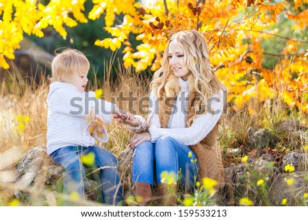 Young mother playing with her daughter in autumn park