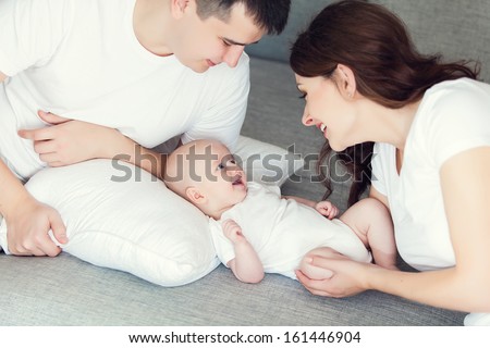 Mother And Father Playing With Their Cute Baby On The Couch At Home