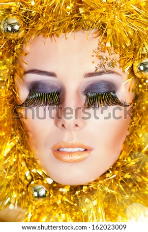 Christmas makeup of beautiful woman with gold tinsel on face