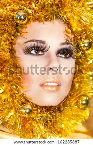 Christmas makeup of beautiful woman with gold tinsel on face