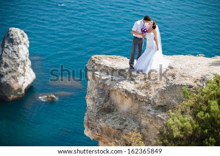 wedding couple stands on a cliff above blue sea