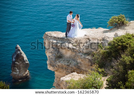 wedding couple stands on a cliff above blue sea
