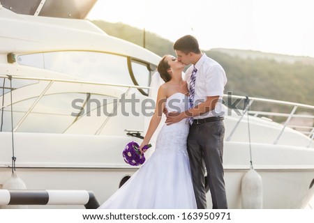 Beautiful bride and groom wedding couple near sea yacht. Happy newlywed couple at wedding. Cheerful married couple standing on the beach.