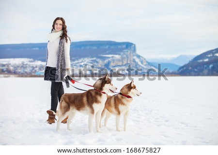 Happy young girl playing with siberian husky dogs in winter park.