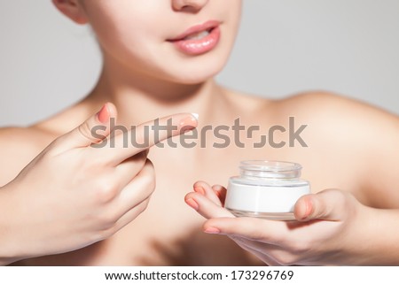Portrait of a beautiful young woman applying face cream against a gray background