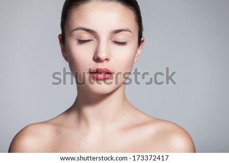 Head and shoulder shot of a beautiful young woman in the nude with eyes closed over gray background