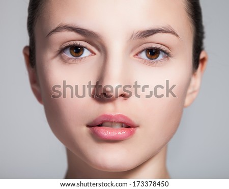 Closeup of a naturally beautiful woman with flawless skin gazing at you on gray