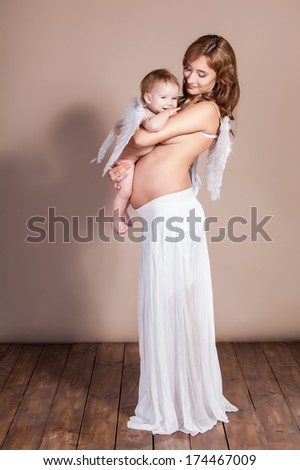 A pretty pregnant woman playing with her daughter with angel wings