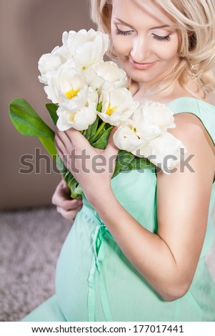 Pregnant woman wearing long green dress, holding in hands bouquet of  flowers, new life concept