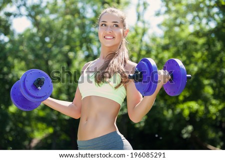 Young sport woman exercising with heavy steel dumbbell - outside in nature. Fitness exercise.