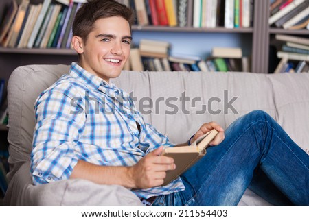 Handsome young man relaxing at home on a sofa in the living room reading a book or studying
