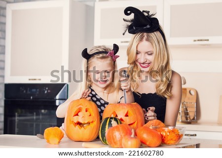 Kid on Halloween party making carved pumpkin with a little help from her mother Kid on Halloween party making carved pumpkin with a little help from her mother