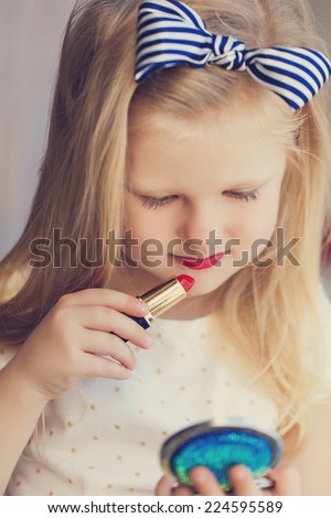 Little girl with lipstick and mirror. Makeup in studio